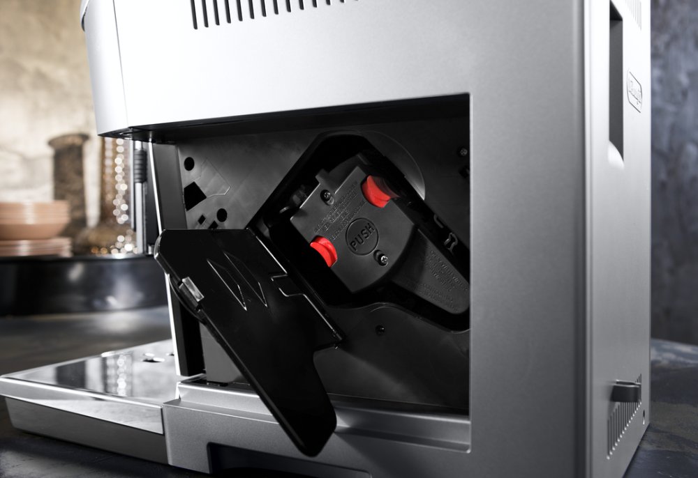 DeLonghi kávovar – otvorený bočný kryt s viditeľnou sparovacou jednotkou a červenými uvoľňovacími tlačidlami